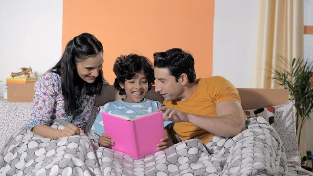 Caring young mom and dad reading a storybook with their adorable child at home. Closeup shot of a sweet little kid enjoying spending his free time together with his parents - family bonding and rel...