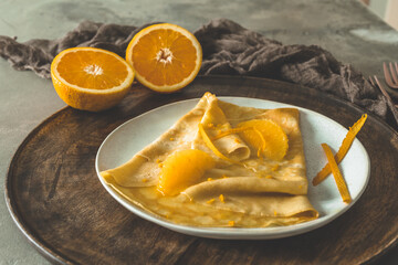 Crepe Suzette, french thin pancake with orange sauce and fruits, on a wooden plate on gray concrete background