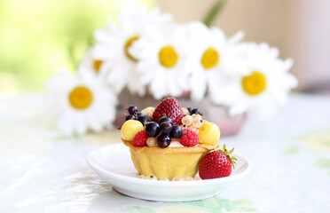 Cupcake cake tartlet with cream and berries - raspberries, strawberries, currants, cherries on a white plate on a table in the garden