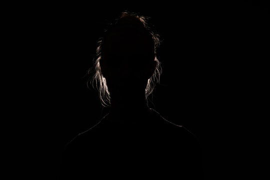 backlit portrait silhouette of unrecognizable woman hiding face and identy in the dark shadow