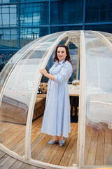 woman in a blue dress stands in a cafe in the shape of a igloo on roof. 