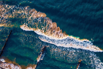 Aerial top view of breakwater with big wave of ocean, clean blue water around beach