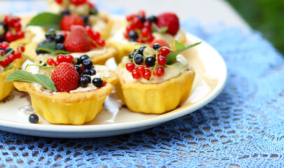 Cupcake cakes with meringues and fresh berries  strawberries, raspberries, blueberries, red white currants, mint leaves on a large plate on a knitted blue tablecloth in the garden. Summer dessert