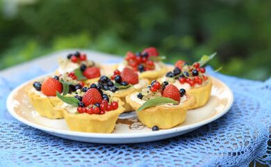 Cupcake cakes with meringues and fresh berries  strawberries, raspberries, blueberries, red white currants, mint leaves on a large plate on a knitted blue tablecloth in the garden. Summer dessert