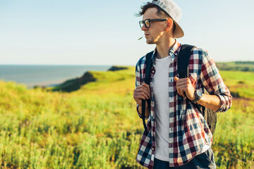 young man, in glasses and in a cap with a backpack, hiking and enjoying the mountain landscape, adventure man hiking in the desert mountains