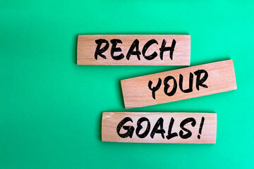 Reach Your Goals! words made on wooden building blocks green background.