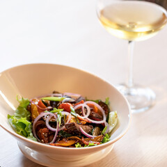 Bowl of fresh vitamin salad and glass of white wine on blurred background. High key. Copy space. Soft focus.