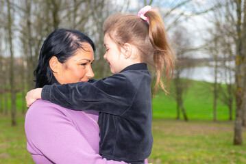 Beautiful mother and daughter play hugs in a spring park nature in profile looking at each other.