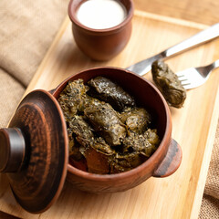 Classic dolma, Rolls wrapped in grape leaves. Close-up shot. Pot of hot stewed dolma on wooden background. Soft focus.