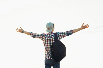 Young man with a backpack standing with raised hands on the top of the mountain, against the background of blue sky