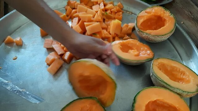 The man uses a knife to split the orange melon, muskmelon, cantaloupe on a steel plate, Muskmelon Juice or kharbuj, kharbuja extract in a steel plate, Cantaloupe