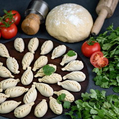 Raw dumplings and ingredients for their preparation, parsley and tomatoes on black table. Close-up...