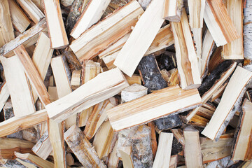 Lots of frozen, chopped birch logs. The firewood is sawn and split. The logs lie chaotically and piled up in a heap. A dark core is visible on the split wood. A texture or background.