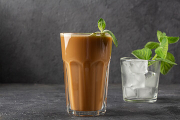 Ice coffee with mint and milk. Big glass of coffee cocktail and glass with ice cubes. Cool refreshment summer drink on dark background in law key. copy space for text.