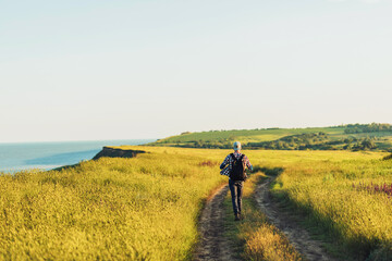 Active tourist, a man with a briefcase in nature, a hipster in a cap is walking along a path on a green hill, healthy lifestyle
