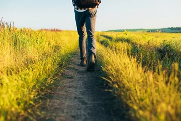 Fotobehang Actieve toerist, een man met een koffertje in de natuur, een hipster met een pet loopt langs een pad op een groene heuvel, een gezonde levensstijl © Shopping King Louie
