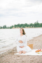 Young beautiful pregnant woman in a beautiful dress near the sea. Picnic. Watermelon.