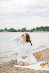 Fototapeta na wymiar Young beautiful pregnant woman in a beautiful dress near the sea. Picnic. Watermelon.