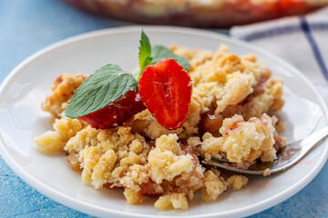 Home сooking. Rhubarb or Strawberry crumble, gluten free crisp in baking dish. Summer dessert on plate on blue background