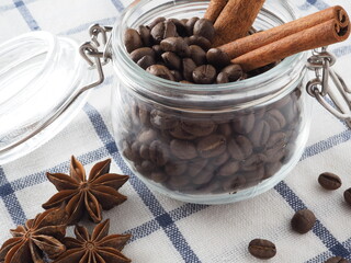 Coffee beans in a jar, cinnamon and star anise on the background of a light napkin