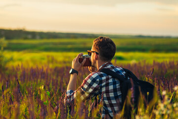 Young male tourist, in sunglasses, with a camera, in nature, spending time in a hike, on the field