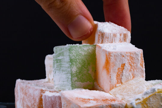 Man taking a Turkish Delight on black background. Ramazan bayrami (eid al fitr) and Kurban bayrami (eid al adha) background photo. Turkish delight (lokum). Eid mubarak - iyi bayramlar