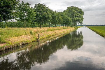 Dutch drainage canal Koningsvliet on a cloudy and windless day in the beginning of the summer season. The photo was taken at the village of Elshout, municipality of Heusden, province of North Brabant.