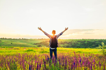 Fototapeta na wymiar Traveler with raised hands standing on a hill in green grass and enjoying a majestic sunset, Successful man enjoying triumph