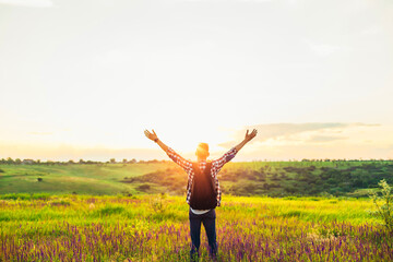 Traveler with raised hands standing on a hill in green grass and enjoying a majestic sunset,...