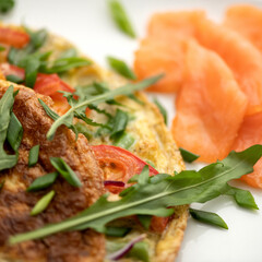 Omelet with arugula and red fish on blurred background. Close-up shot. Morning mood, breakfast. Soft focus.