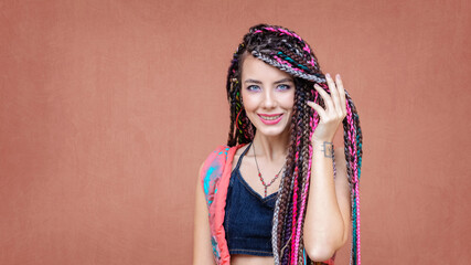 Happy hispanic girl with braids and tattoo smiling at camera outdoors with colorful background