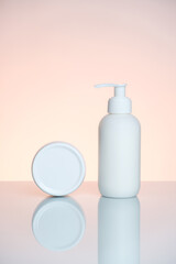 Hand cream in a bottle and jar on a light pink background with reflection.