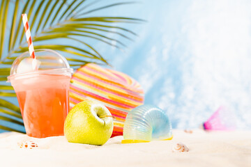 Summer travel, leisure and holiday background - picnic with cold drink, fresh fruit, sun hat and beach games on hot sunny sandy beach with palm, bright ocean view. Vacation on seaside coast.