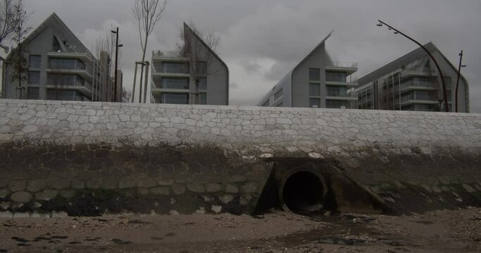 Sewer tunnel exit on the beach. Modern buildings on the back. Pollution. Urban city