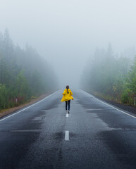 A girl running trough a foggy road in a yellow raincoat