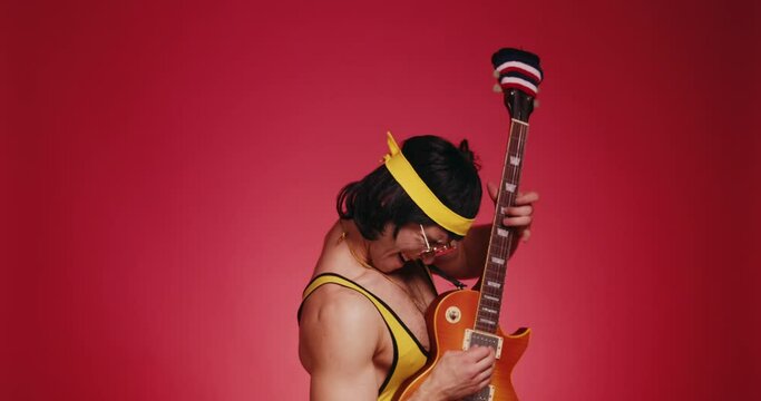 Funny retro athlete man in yellow tracksuit and sunglasses from 80's with guitar feels herself like a rock star isolated on red background. Retro sport hipster show off and posing in front of camera.