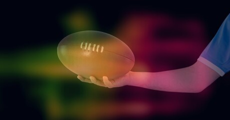Composition of glowing yellow and red blur over arm of rugby player holding rugby ball, on black