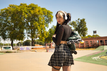 Young girl with pigtails, punk style, white headphones and inline skates hanging from the shoulder...