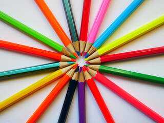 Colored pencils on a white background radiate rays to the sides. They are closed with a rod in the center. 