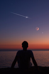 Silhouette of a man looking at the Moon and stars over sea ocean horizon. © astrosystem