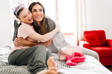 Woman and her daughter with down syndrome hugging while sitting on bad