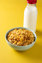 Corn flakes in a blue bowl and milk on yellow background	