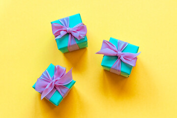 Three turquoise present boxes with bow on yellow background. Top view, flat lay