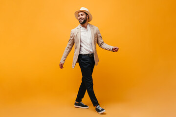 Fototapeta na wymiar Man in hat and stylish outfit moving on orange background