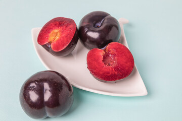 On a white saucer is a large plum, cut in half, and next to it is a whole plum. The pulp of red berries. Close-up.