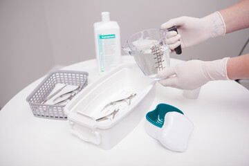 Fototapeta na wymiar Manicurist pouring liquid sterilizer into container with nail nippers