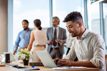Successful leaders build successful teams. Businessman Using Laptop At Desk In Busy Office. Serious dark-skinned young office manager works with different reports and table laptop 