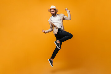 Fototapeta na wymiar Handsome guy in black pants and beige jacket jumps on orange background