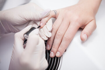 Unrecognizable woman having base coat applied on nails by manicurist