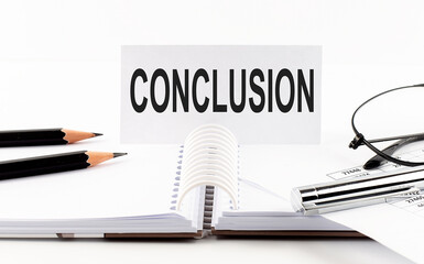 CONCLUSION on paper card,pen, pencils, glasses,financial documentation on table - business concept